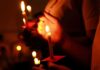 Ten Bodies, One Rotten System Hands holding lit candles in a dark setting