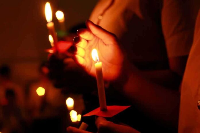 shutterstock_1030954108 Hands holding lit candles in a dark setting