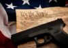 Handgun on U.S. Constitution with American flag backdrop