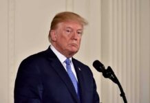 Massive Security For Trump’s Golf Drop-In man in suit at a podium