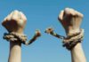 Hands breaking free from rope bindings against a clear blue sky