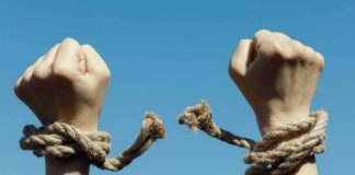 Hands breaking free from rope bindings against a clear blue sky