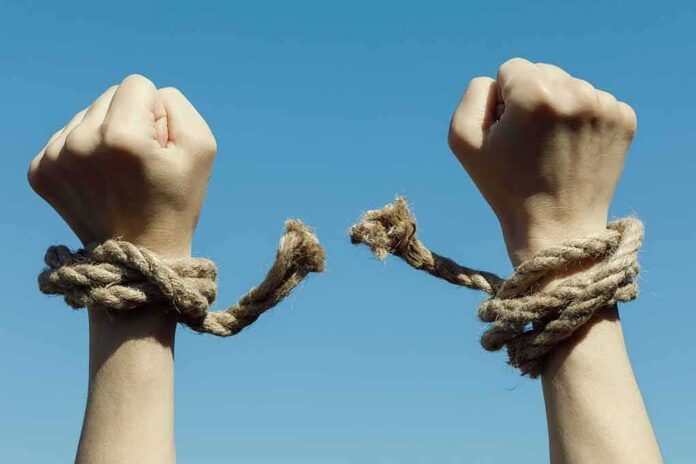shutterstock_1082949368 Hands breaking free from rope bindings against a clear blue sky