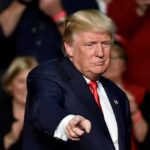 GOP Rumble: Trump Freezes Out Thune man in suit pointing toward the camera at an event