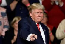 GOP Rumble: Trump Freezes Out Thune man in suit pointing toward the camera at an event
