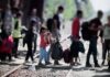 Massive Kid Facility Tests Court Limits People with bags walking along railway tracks