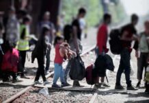 Massive Kid Facility Tests Court Limits People with bags walking along railway tracks