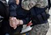 Officers detain a person with hands cuffed behind their back