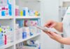 Trump Price Gambit Upends Dingell Narrative Pharmacist using a tablet in front of stocked pharmacy shelves