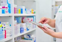 Pharmacist using a tablet in front of stocked pharmacy shelves