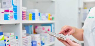 Pharmacist using a tablet in front of stocked pharmacy shelves