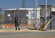 Security guard at chain-link gate of fenced facility