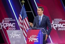FBI Chaos Clouds Kirk Assassination Speaker in suit at CPAC podium on stage