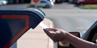 Hand mailing an envelope into a blue mailbox