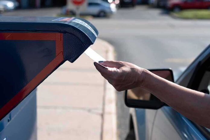 Hand mailing an envelope into a blue mailbox