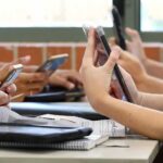students' hands using smartphones at a classroom table