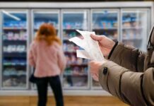 Person holding grocery receipts in front of supermarket freezer aisle