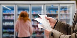 Person holding grocery receipts in front of supermarket freezer aisle