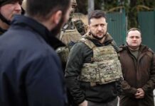 man in tactical vest stands with group outdoors