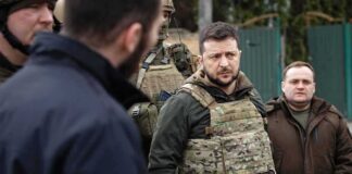 man in tactical vest stands with group outdoors