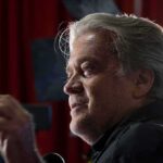 Bannon’s PM Megaphone Shapes Washington man speaking at a microphone in a dimly lit setting