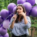 Egg-Freezing Drama Hijacks The Discourse Woman speaking into a microphone at an outdoor event with purple balloons