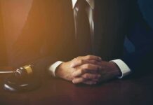 AI Fake Citations Wreck Deutsche Bank In Court person in suit with hands clasped at a desk beside a gavel