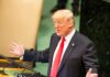 Donald Trump speaking at a podium with arms outstretched