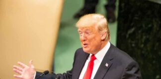 Donald Trump speaking at a podium with arms outstretched