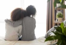 Two people sitting on a bed with arms around each other