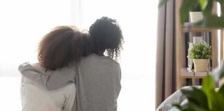 Two people sitting on a bed with arms around each other