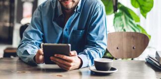 Man in blue shirt using a tablet at a cafe table