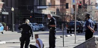 Police officers detain a seated man on a city sidewalk