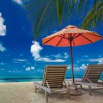 Two lounge chairs under an orange umbrella on a tropical beach