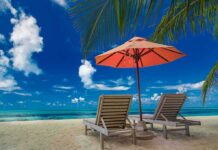 Two lounge chairs under an orange umbrella on a tropical beach