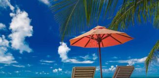 Two lounge chairs under an orange umbrella on a tropical beach