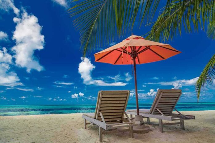 shutterstock_1931633669 Two lounge chairs under an orange umbrella on a tropical beach