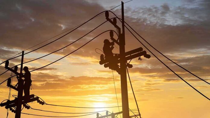 shutterstock_1979642963 Utility workers on power poles at sunset