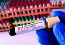 Gloved hand holding an STI test tube labeled positive