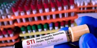 Gloved hand holding an STI test tube labeled positive
