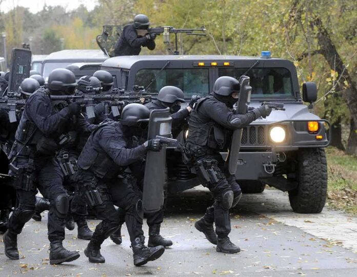 Tactical police team advances from armored vehicle with shields and rifles