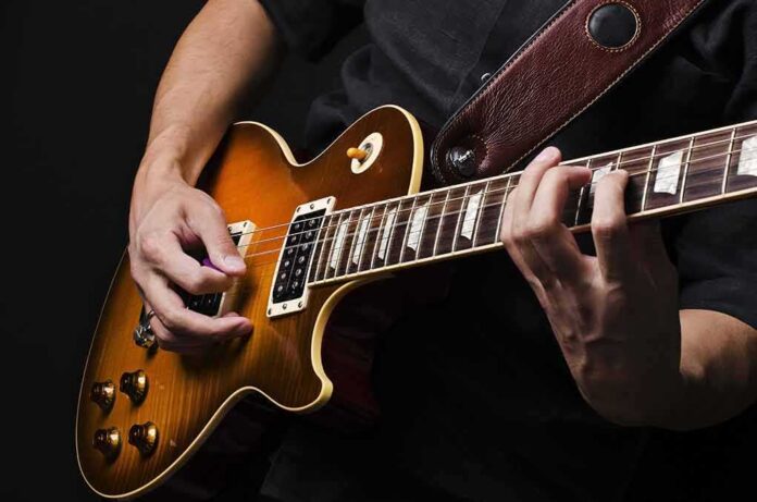 shutterstock_92514370 Electric guitar player strumming and fretting on a sunburst Les Paul style guitar