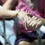 Elderly person’s hands resting on a hospital bed rail