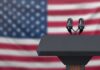 Podium with microphones in front of a blurred American flag