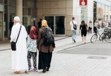 UK Hands Out Hijabs – Border Welfare Or Welcome Pack? Three people walking on a city sidewalk