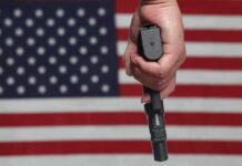 Hand holding a handgun in front of an American flag