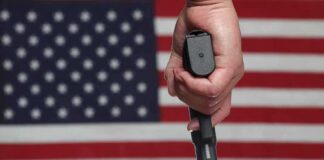 Hand holding a handgun in front of an American flag