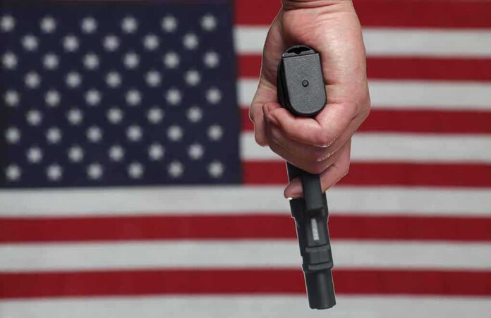 shutterstock_141984028 Hand holding a handgun in front of an American flag