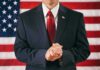 Man in suit with red tie standing before American flag