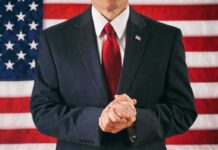 Man in suit with red tie standing before American flag